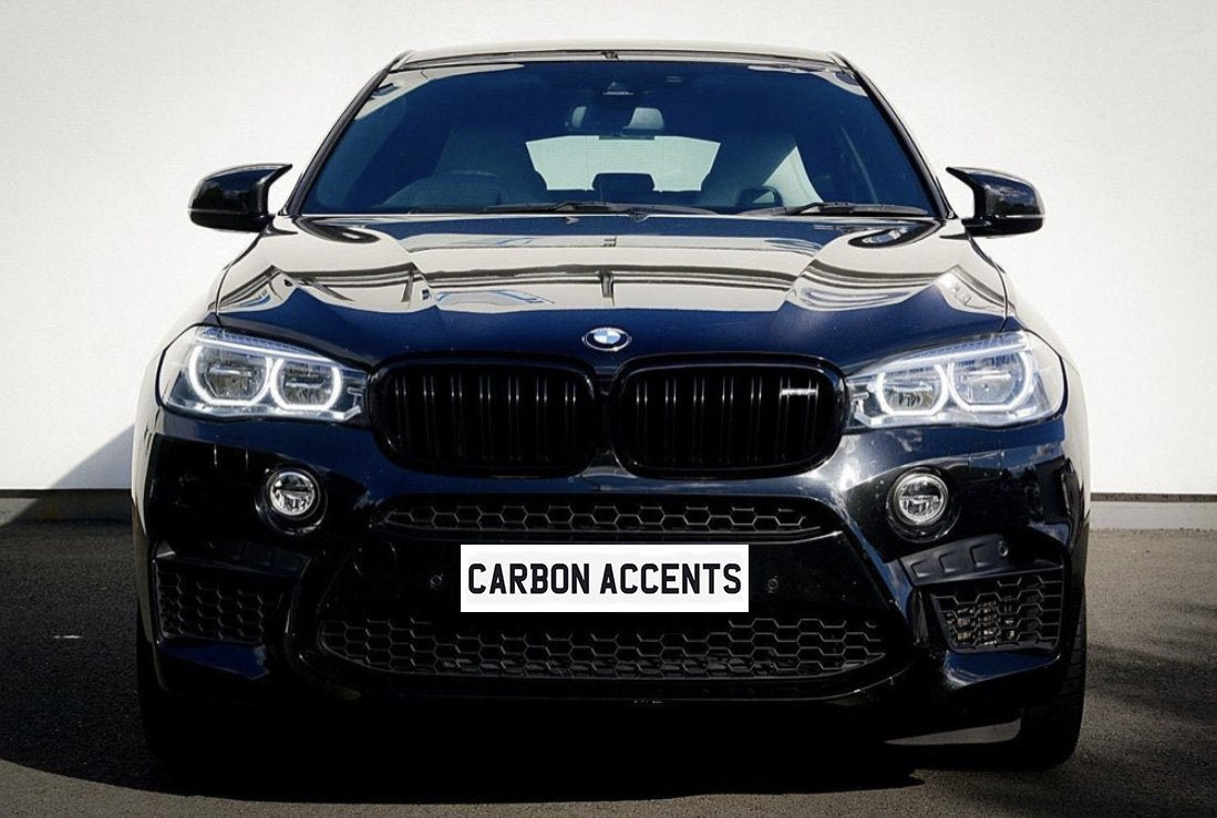 A black car with prominent headlights and grille is parked on a street. The license plate reads "CARBON ACCENTS." The light reflects off its shiny surface.