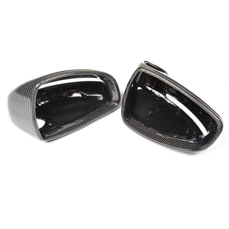 Two glossy black carbon fiber side mirror covers rest side by side, displaying their smooth, reflective surfaces against a plain white background.