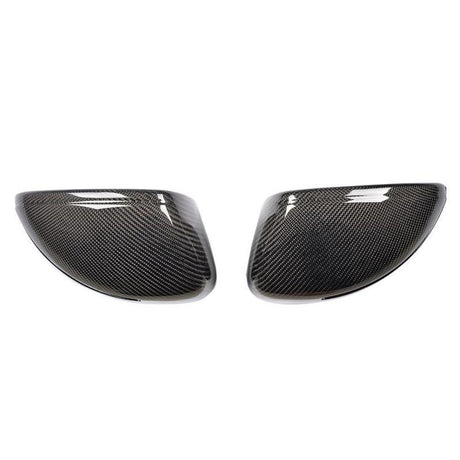 Two carbon fiber wing mirror covers are side by side, angled towards each other, against a plain white background. The covers have a glossy finish with a detailed woven pattern.