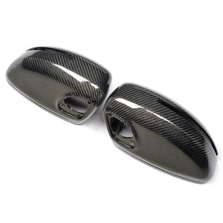 Two glossy carbon fiber side mirror covers rest on a white background, showcasing a sleek, modern design with visible weave patterns and mounting holes.