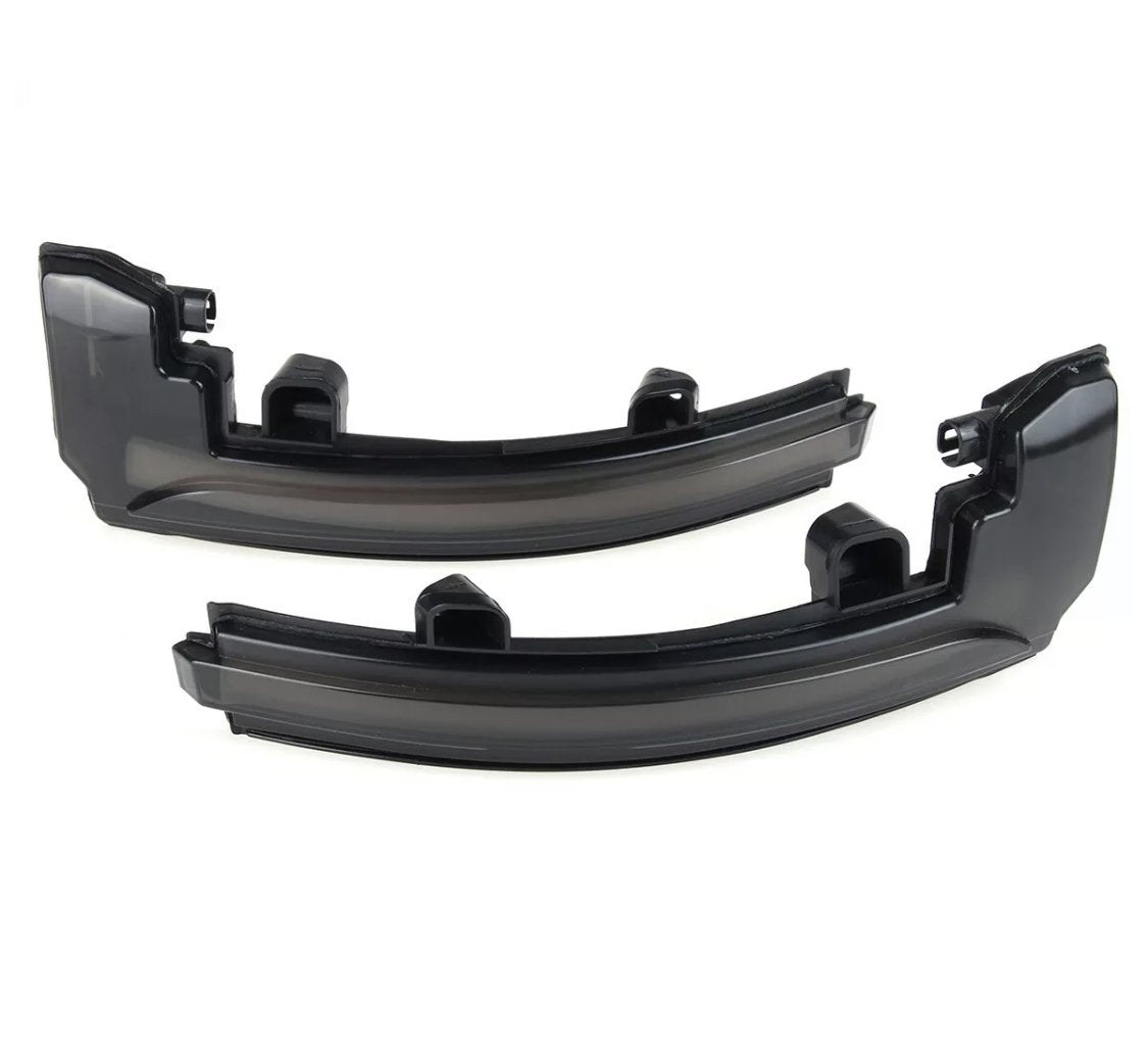 Two black plastic automotive light covers lie side by side, appearing glossy and curved, intended for vehicle use in a neutral, light-colored space.