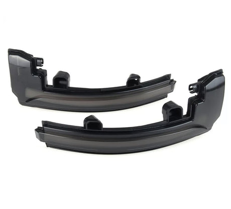 Two black plastic automotive light covers lie side by side, appearing glossy and curved, intended for vehicle use in a neutral, light-colored space.