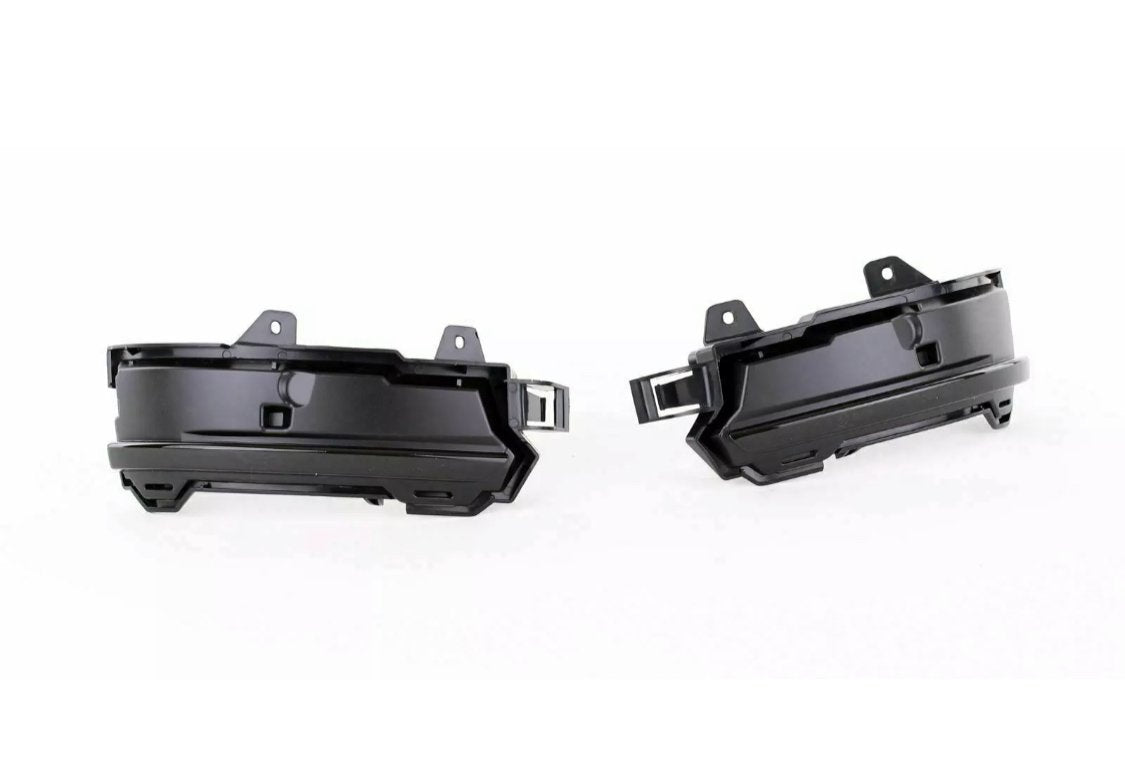 Two black plastic automotive parts, likely fog light housings, are positioned side by side facing outward. They feature mounting brackets and an angular design, set against a plain white background.