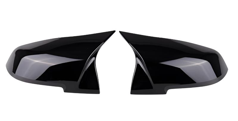 Two glossy black side mirror covers are positioned facing each other. They are streamlined, reflecting light subtly, against a plain white background.
