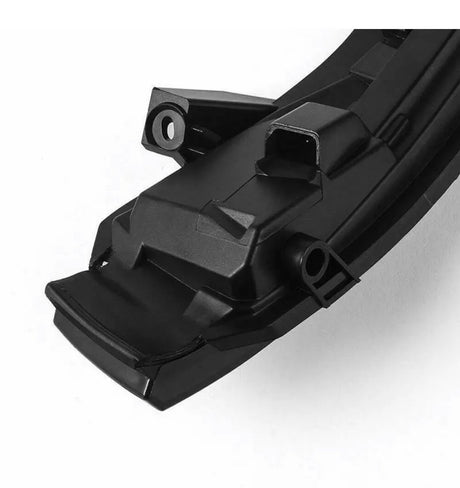 A black, angular, plastic automotive component with a rectangular connector port sits on a smooth, white background, featuring mounting points and a sleek, modern design.