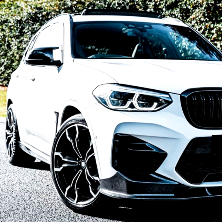 A white SUV with sporty black wheels is parked on a road, surrounded by lush green trees in a sunny environment.