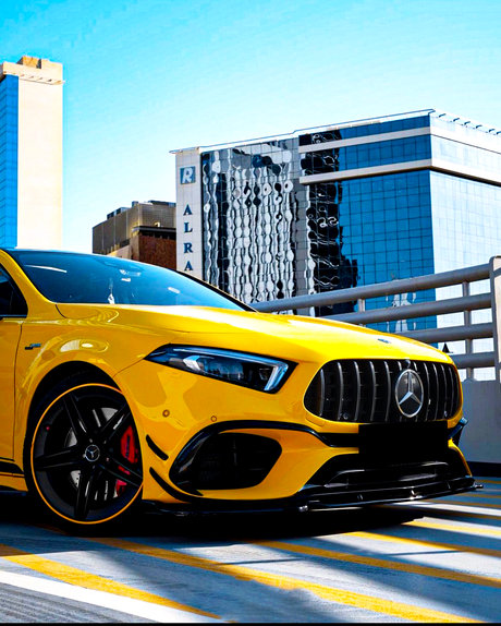 A yellow sports car is parked on a rooftop parking lot with a cityscape of modern glass buildings under a clear blue sky.