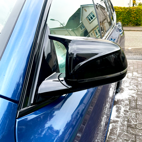 A black side mirror is attached to a blue car, parked on a wet, sudsy driveway beneath residential houses.