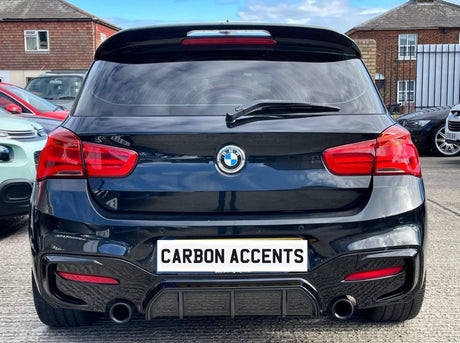 A black BMW car is parked, displaying a license plate reading "CARBON ACCENTS." Surrounding the vehicle are other parked cars and brick buildings under a cloudy sky.
