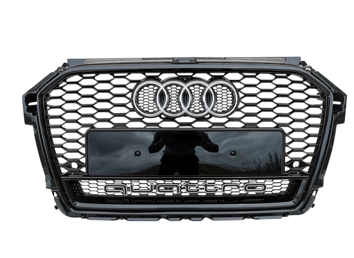 A black car grille with a honeycomb pattern displays the Audi logo (four rings) at the top center. Below, "quattro" is prominently featured. It’s outdoors with a reflection of a person.
