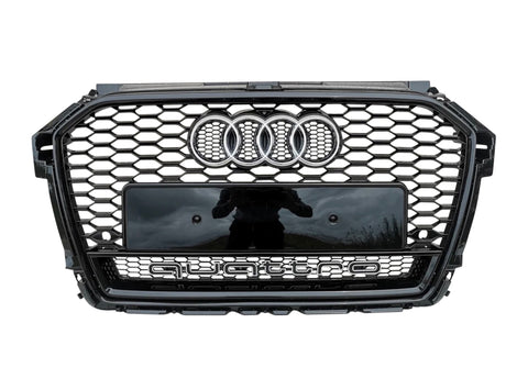 A black car grille with a honeycomb pattern displays the Audi logo (four rings) at the top center. Below, "quattro" is prominently featured. It’s outdoors with a reflection of a person.