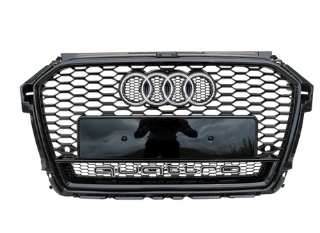 A car grille features a honeycomb pattern, with the Audi logo and the word "quattro" prominently displayed on a metallic surface, set against a gray background.