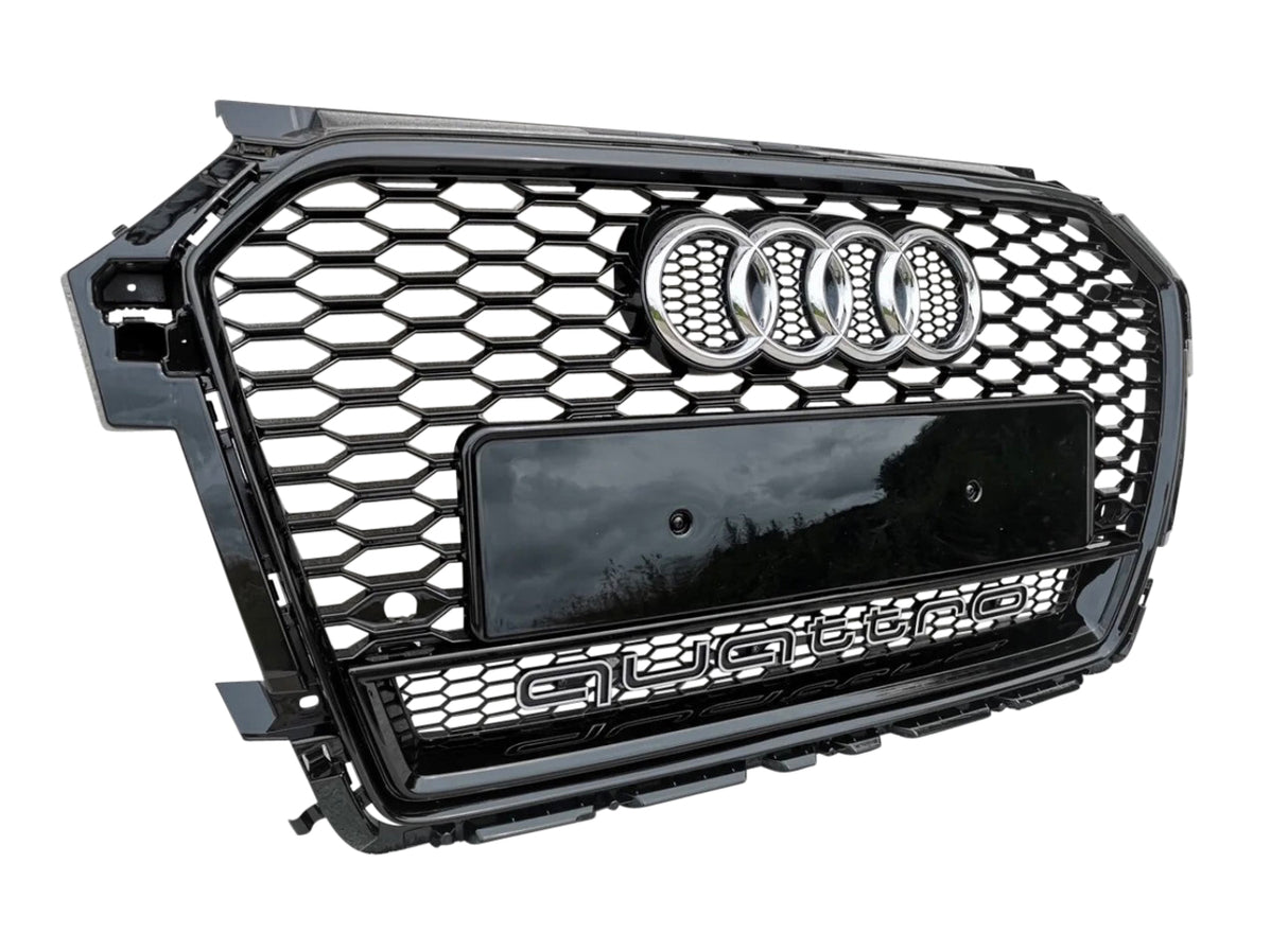 A glossy black car grille with a honeycomb pattern features four interlinked rings and a black plate. "Quattro" is prominently displayed on the lower section. It is isolated against a white background.