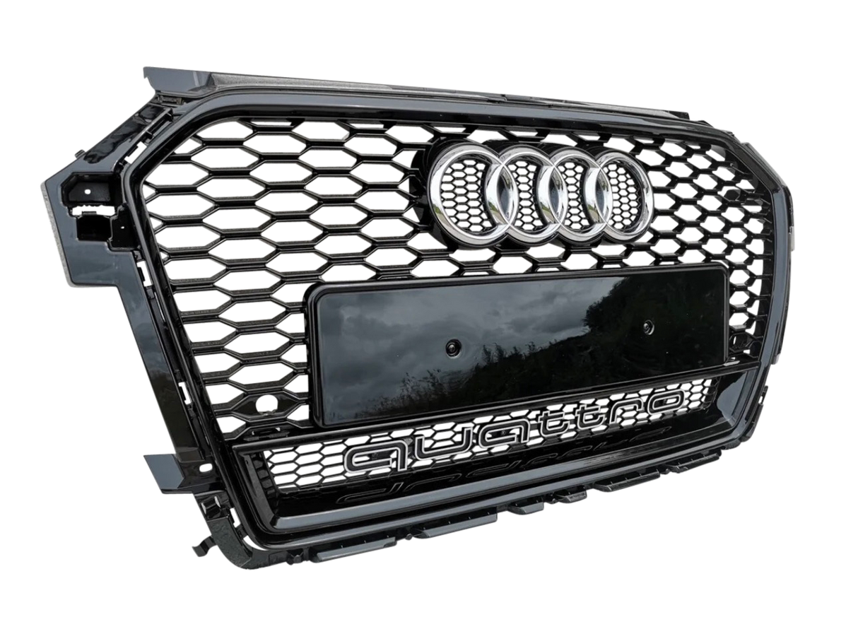 A car grille displays the Audi logo and "quattro" text in a hexagonal pattern with a glossy black finish, positioned against a light gray textured background.