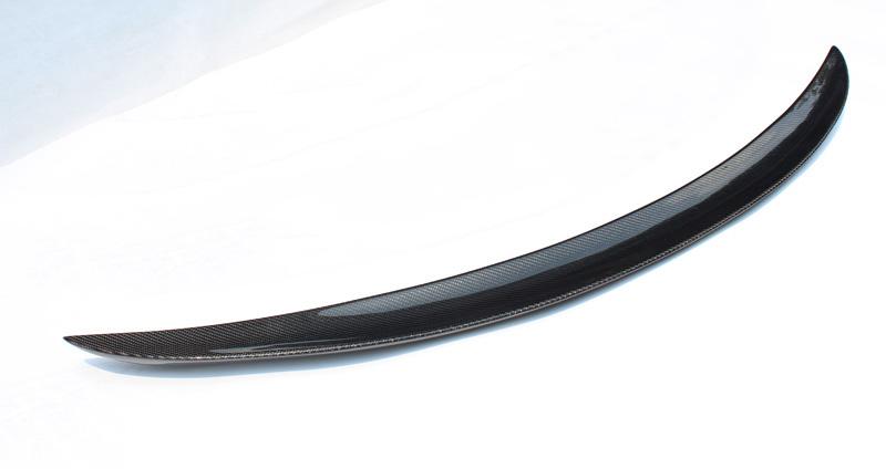 Curved carbon fiber car spoiler resting against a white background, showcasing its sleek, aerodynamic design.