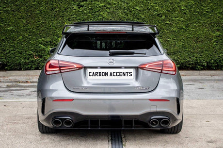A silver Mercedes-Benz hatchback (AMG A 45 S) is parked on concrete. The license plate reads "CARBON ACCENTS," with dense greenery in the background.