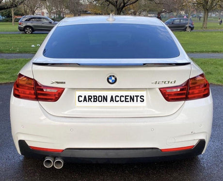 A white BMW 420d is parked on a paved path, with "CARBON ACCENTS" displayed on its license plate, surrounded by green lawns and other parked cars in a park setting.