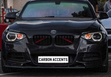 A black car is parked in a lot, featuring illuminated headlights and "CARBON ACCENTS" written on the front. Other vehicles and people are visible in the background.