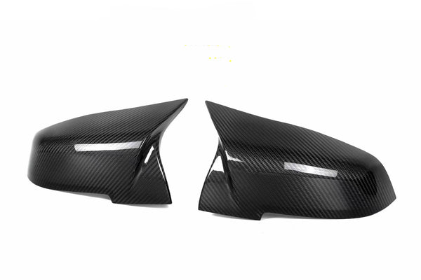 Two black carbon fiber side mirror covers are positioned facing each other against a plain white background, highlighting their sleek, aerodynamic design and glossy finish.