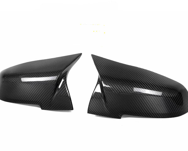Two black carbon fiber side mirror covers are placed on a white background, showcasing their glossy, textured surface and aerodynamic design.