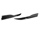 Two glossy, black carbon fiber side skirts with a slight upward curve rest on a white background, showcasing aerodynamic enhancements for vehicles.