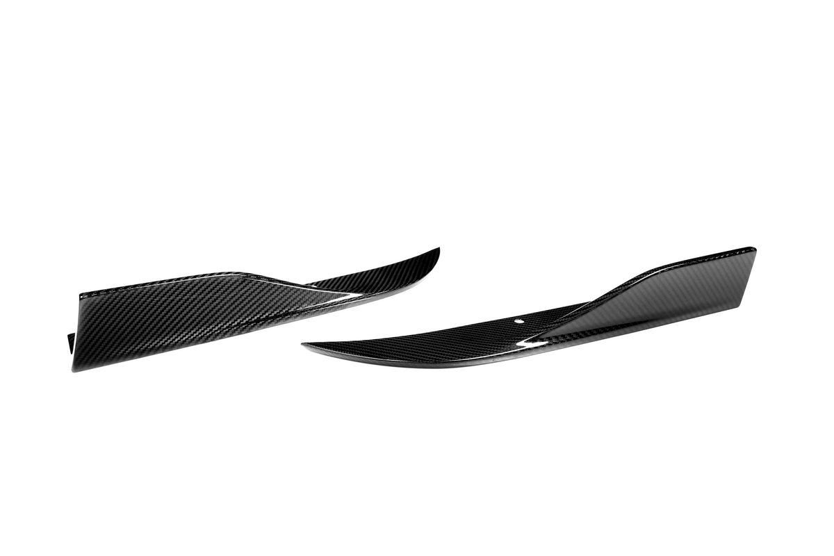 Two glossy, black carbon fiber side skirts with a slight upward curve rest on a white background, showcasing aerodynamic enhancements for vehicles.
