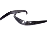 Two curved carbon fiber pieces are positioned parallel on a white background, likely automotive parts, showcasing sleek, aerodynamic lines and a glossy finish.