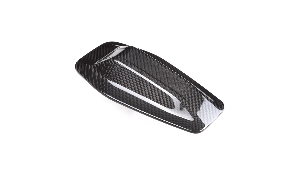 A sleek, carbon fiber car side mirror cover with a glossy finish, resting against a plain white background, highlighting its aerodynamic design and textured pattern.