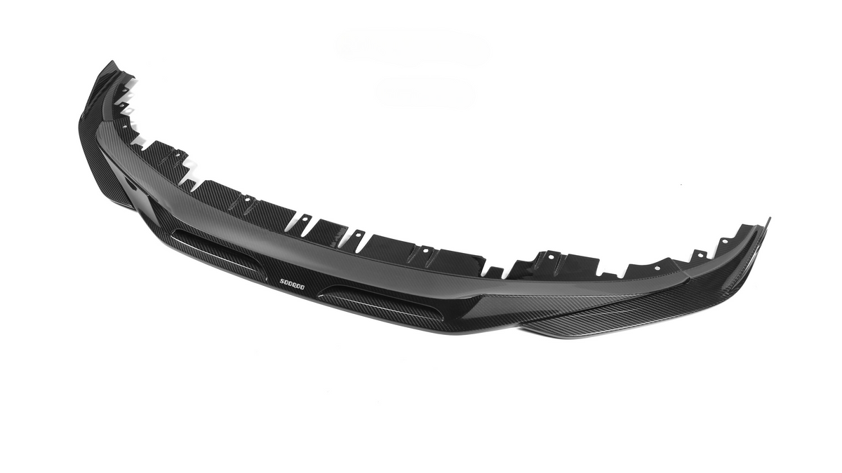 A black carbon fiber car front splitter with several attachment points lies against a plain white background. Text on the splitter reads "SODOCOO."