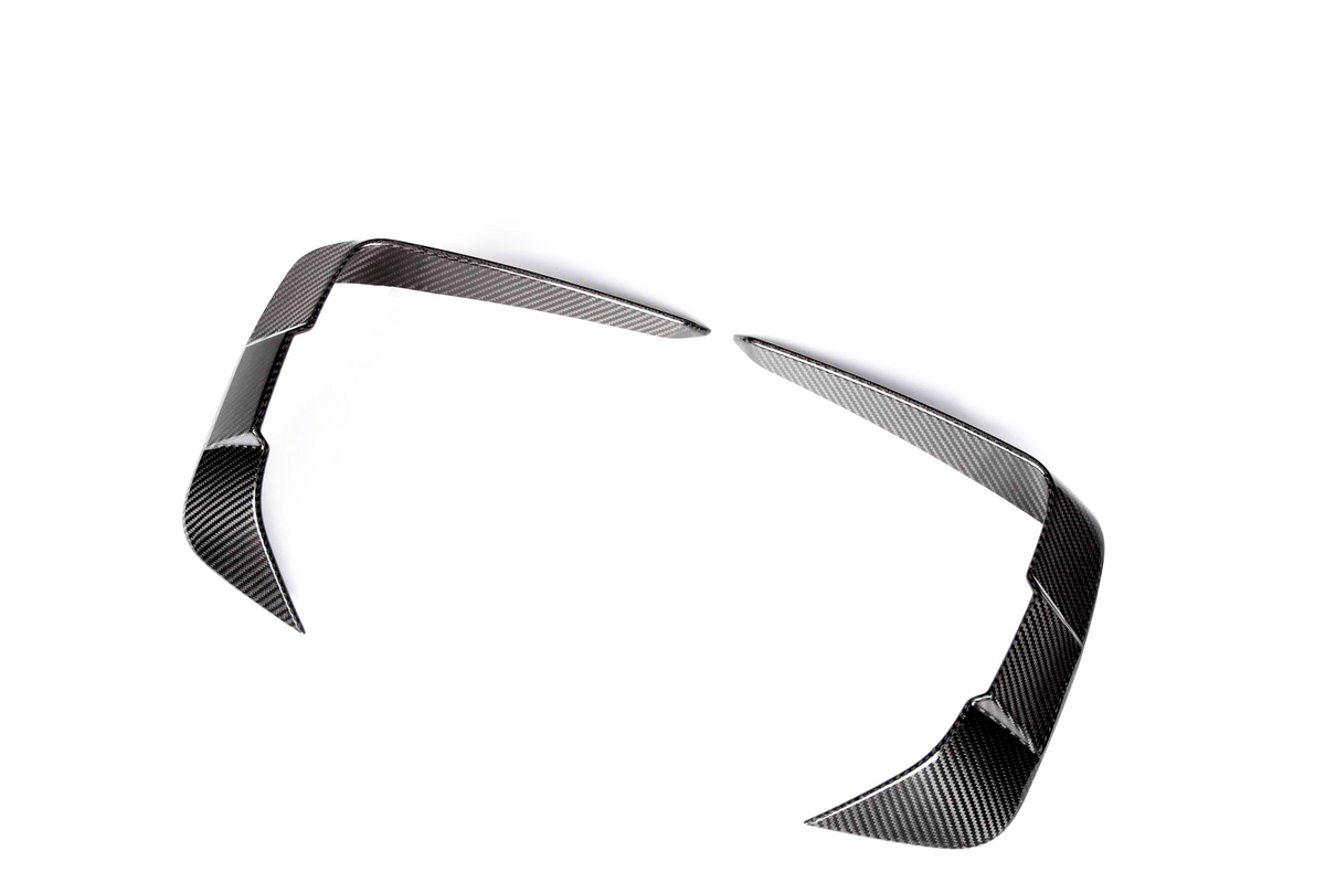 Curved carbon fiber car parts, resembling aerodynamic fins, rest apart on a white background, showcasing a sleek, reflective surface pattern.