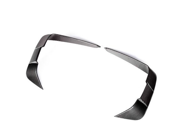 Curved carbon fiber car parts, resembling aerodynamic fins, rest apart on a white background, showcasing a sleek, reflective surface pattern.