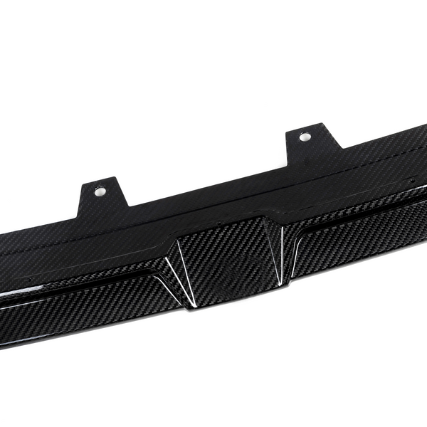 A carbon fiber car diffuser lies flat, showing textured pattern and mounting brackets, set against a plain white background.