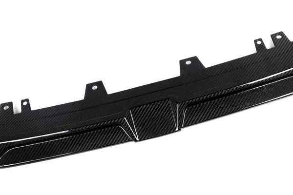 A carbon fiber car diffuser lies flat, showing textured pattern and mounting brackets, set against a plain white background.