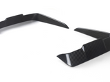 Two carbon-fiber vehicle splitters angled upward, placed on a white surface, likely designed for aerodynamics, showing a modern, sleek pattern.