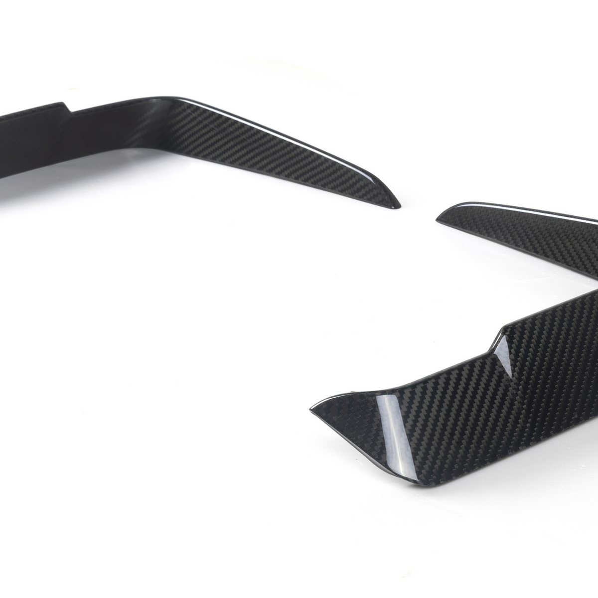 Two carbon-fiber vehicle splitters angled upward, placed on a white surface, likely designed for aerodynamics, showing a modern, sleek pattern.
