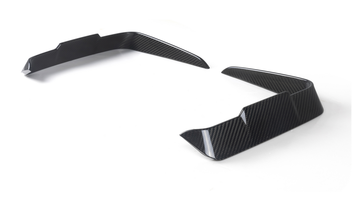 Two carbon-fiber vehicle splitters angled upward, placed on a white surface, likely designed for aerodynamics, showing a modern, sleek pattern.