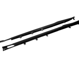 Two black carbon fiber car side skirts with attachment brackets lie against a plain white background, emphasizing their sleek design and aerodynamic purpose.