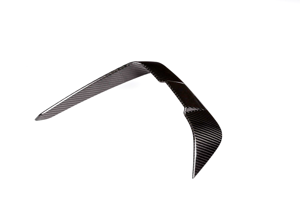 A shiny carbon fiber boomerang rests in a balanced, upright position against a plain white background, displaying a smooth, woven texture.