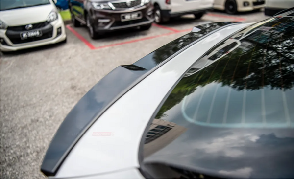 A glossy car, parked, reflects trees and sky on its rear window. Other vehicles are parked nearby in an outdoor lot.