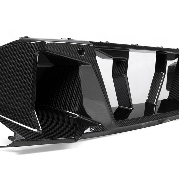 A carbon fiber car part with aerodynamic, angular features rests on a smooth white background, emphasizing its sleek, glossy finish and intricate texture.