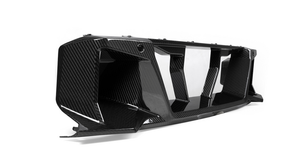 A carbon fiber car part with aerodynamic, angular features rests on a smooth white background, emphasizing its sleek, glossy finish and intricate texture.