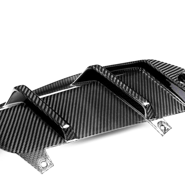 Carbon fiber car part with raised fins, resting on a white surface, featuring a glossy, patterned design and mounting holes.