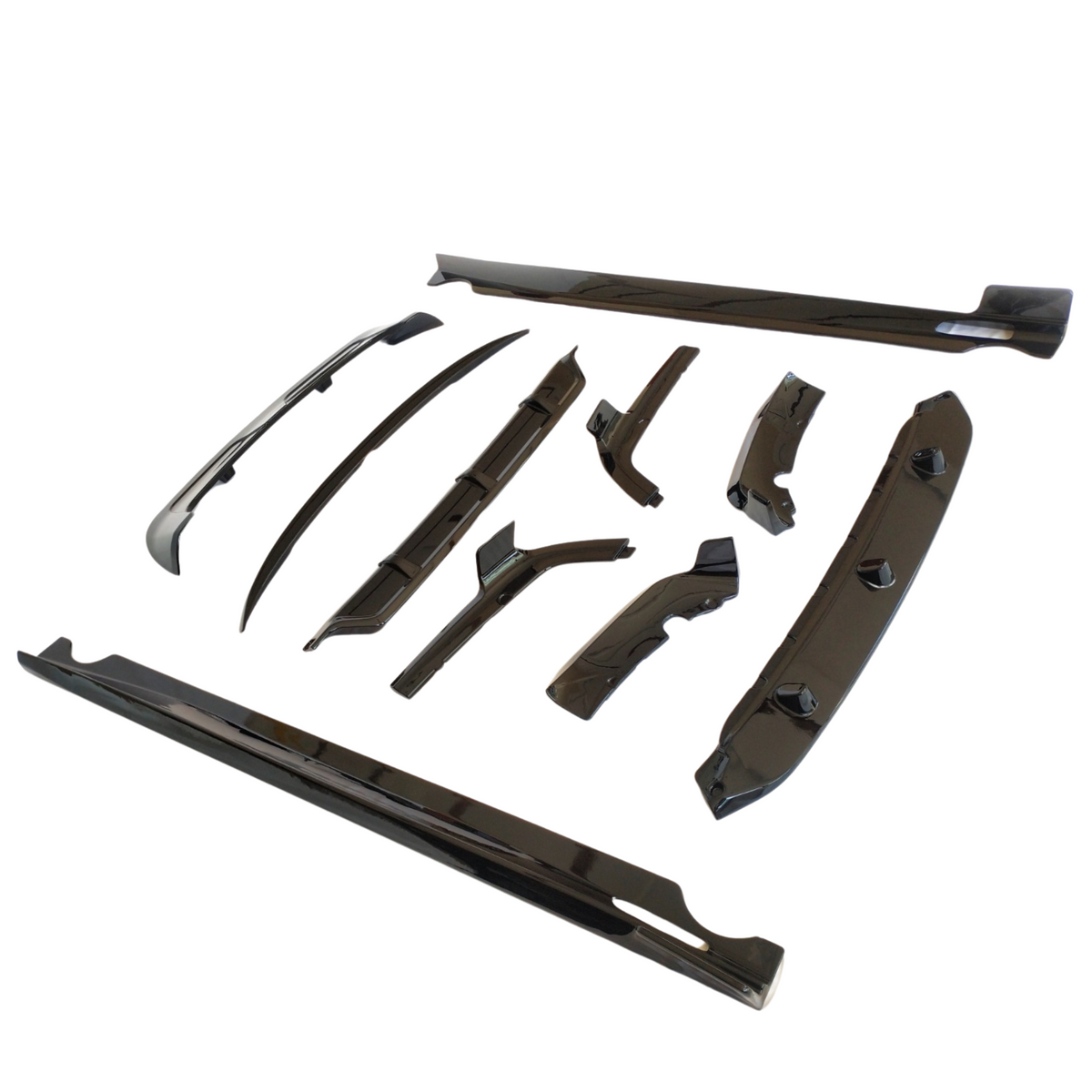 Car body kit components arranged on a white surface, including various sleek, black aerodynamic parts such as side skirts, spoilers, and diffusers, designed to enhance vehicle performance and appearance.