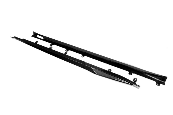Two elongated, black carbon fiber side skirts with mounting brackets lie parallel on a plain white background, designed for automotive use, enhancing aerodynamic performance.