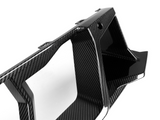 A sleek, black carbon fiber car part with geometric design, featuring sharp angles and contours, is placed against a plain white background.