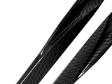 Glossy carbon fiber strips with a distinctive woven pattern lie diagonally on a white background, reflecting light and emphasizing their texture and sleek appearance.