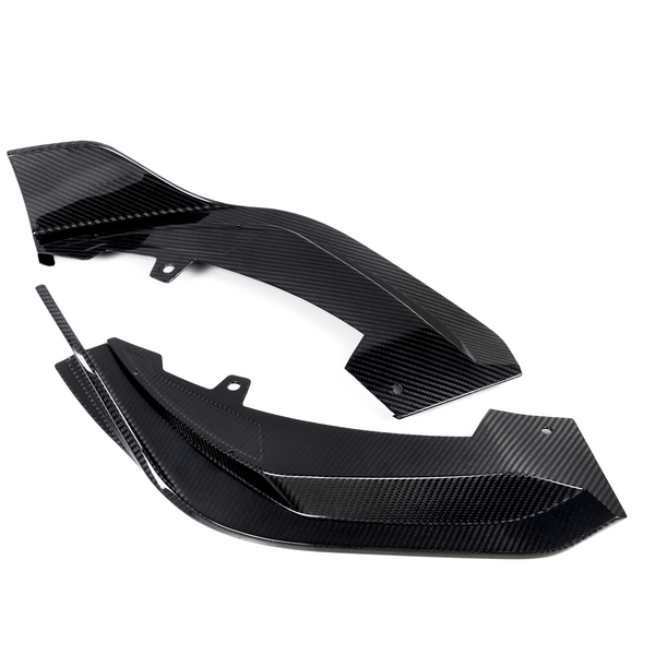 Two black carbon fiber components rest on a white background, featuring a glossy, textured surface with angular edges and mounting holes, suggesting automotive or aeronautical applications.