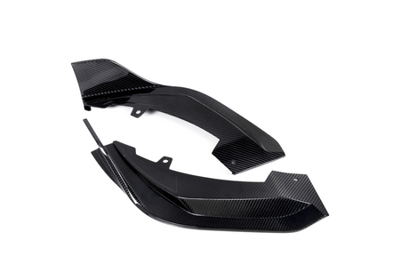 Two black carbon fiber components rest on a white background, featuring a glossy, textured surface with angular edges and mounting holes, suggesting automotive or aeronautical applications.