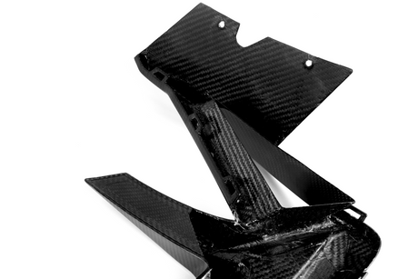 A carbon fiber automotive component with sleek, angular design lays on a plain white background, showcasing its lightweight and durable structure.