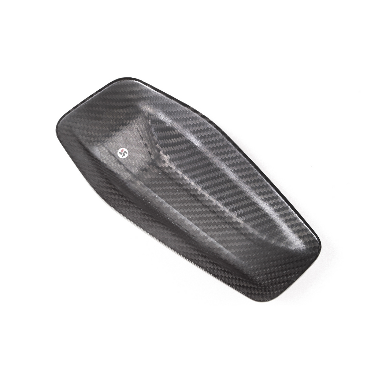 A carbon fiber panel with textured weave pattern lies flat against a plain white background, featuring a small, circular decal near its center.